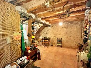 Cette pièce au charme rustique se distingue par ses poutres apparentes, ses murs en pierre, son sol en terre cuite, sa décoration vintage éclectique, ses cloisons tressées, ses étagères ornées de poteries et ses divers objets de la vie quotidienne, créant ainsi une atmosphère chaleureuse.