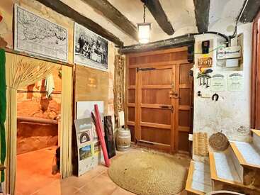 Cette entrée rustique et chaleureuse se compose d'une porte en bois, de poutres apparentes, de cartes anciennes, de certificats, d'un tapis en paille, de matériel artistique, d'un panier en osier, d'une petite marche et de tons chauds et naturels.