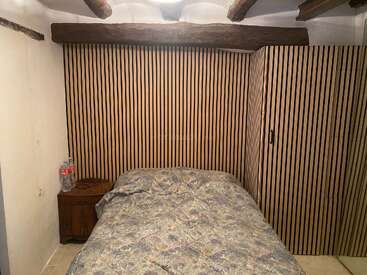 Cette chambre confortable est équipée d'un lit recouvert d'un couvre-lit à motifs floraux, de lambris en bois rayés, de poutres apparentes, d'une armoire et d'une table de chevet sur laquelle sont posées des bouteilles d'eau.