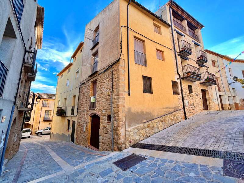 Une ruelle pittoresque bordée de charmants bâtiments en pierre et en stuc, avec des balcons en fer forgé et des façades rustiques, sous un ciel d'un bleu éclatant, dans une petite ville pleine de charme.