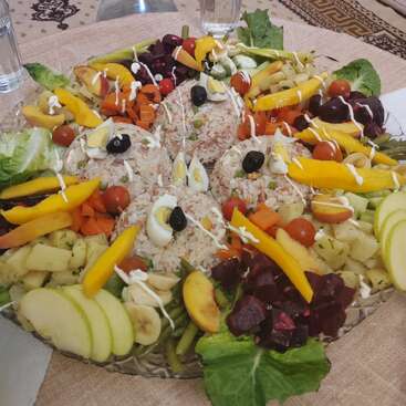 Un plat vibrant composé de monticules de riz garnis d'olives et d'œufs, entourés de légumes colorés, de fruits, de tomates cerises et de légumes verts feuillus, arrosés d'une vinaigrette crémeuse.