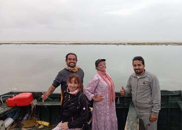 Quatre personnes se tiennent sur un bateau, souriant et posant joyeusement. L'eau calme et le ciel nuageux forment une toile de fond paisible. Deux personnes se donnent le pouce, créant ainsi une atmosphère joyeuse.