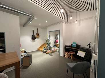 In diesem gemütlichen, modernen Musikzimmer sorgen zwei an der Wand befestigte Gitarren, ein Klavier, sanfte Beleuchtung, ein Stuhl, Pflanzen, bunte Kissen und verspielte Dekoration für eine kreative Atmosphäre.