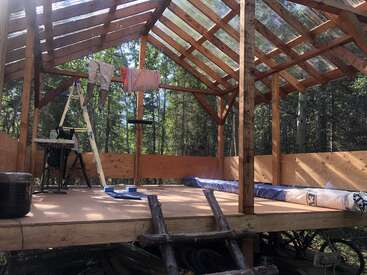L'image représente l'intérieur d'une structure en bois en cours de construction, avec un toit en pente doté de panneaux transparents, entouré d'arbres et d'une échelle sur le côté gauche.
