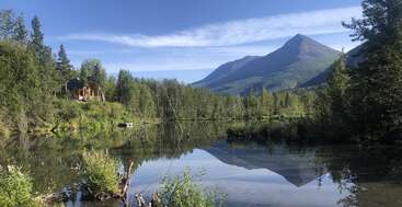 L'image représente un paysage serein avec une étendue d'eau tranquille, entourée d'une verdure luxuriante et d'une chaîne de montagnes majestueuse, évoquant un sentiment de paix et de beauté naturelle.