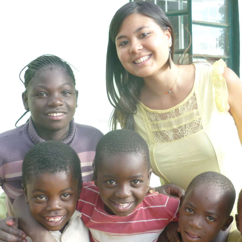The image depicts a woman posing with four children, all of whom appear to be of African descent, in front of a window with a green frame.