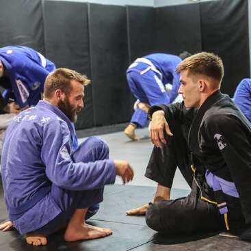 L'image montre un groupe de personnes dans une classe d'arts martiaux, probablement en train de pratiquer le Jiu-Jitsu brésilien, avec des individus portant des uniformes et s'engageant dans diverses poses et mouvements.