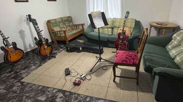 Esta acogedora sala de música cuenta con tres guitarras, un atril con partituras, sofás con cojines, una mesita y pedales de guitarra sobre una alfombra beige.