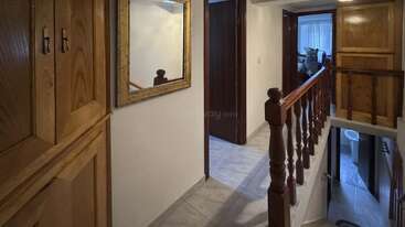 Esta imagen muestra un pasillo interior con armarios de madera, un gran espejo en la pared, suelos de baldosas, barandillas de madera y puertas que conducen a otras habitaciones y a una escalera.