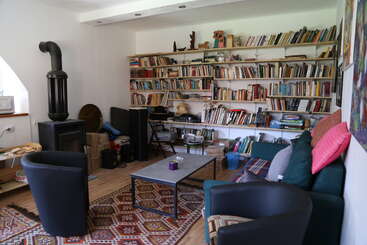 This cozy room features a wood stove, bookshelves filled with books, comfortable seating, a coffee table, colorful rug, soft lighting, and eclectic decorations throughout.