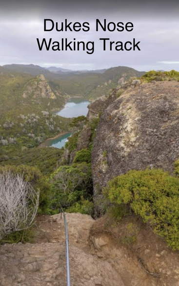 Das Bild zeigt einen Aussichtspunkt am Dukes Nose Walking Track mit Blick auf üppig grüne Hügel, felsige Klippen und einen ruhigen blauen See, der sich unten inmitten der Natur erstreckt.