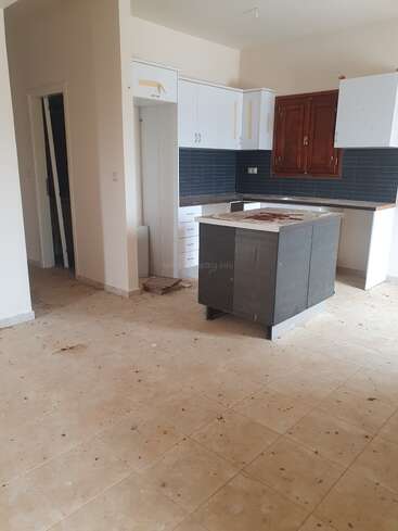 Esta imagen muestra una cocina desordenada e inacabada, con polvo y escombros en el suelo de baldosas. Los armarios y la isla parecen incompletos y faltan puertas.