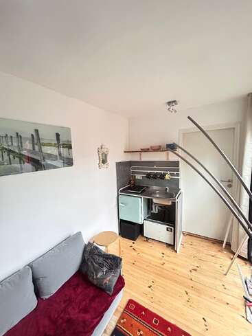 Cette photo montre une petite pièce chaleureuse avec un canapé gris, un parquet, un mini-coin cuisine, des décorations murales, un miroir, une petite étagère et une lumière naturelle éclatante.