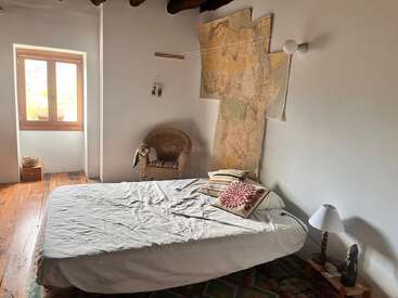 Um quarto aconchegante e minimalista com piso de madeira, cama de casal, cadeira de tecido, travesseiros ecléticos, arte de parede com mapa, luminária pequena e janela clara, exalando charme rústico.