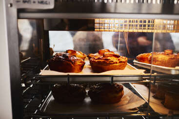 À l'intérieur d'une vitrine de boulangerie, des pâtisseries dorées sont posées sur des plateaux sous un éclairage chaleureux. Les pâtisseries semblent fraîchement cuites et délicieuses, prêtes à être dégustées par les clients.