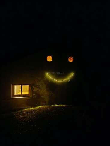 Nachts leuchten an einem Haus zwei runde Fenster und eine geschwungene Lichterkette, die auf der dunklen Fassade wie ein strahlendes Smiley-Gesicht aussehen.