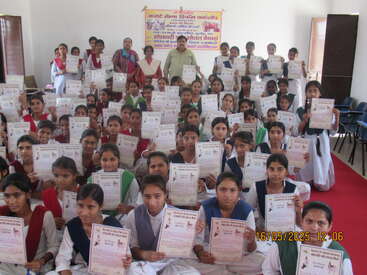 A large group of young women, dressed in school uniforms, proudly display certificates in a classroom setting, celebrating their achievements at a certificate ceremony event.