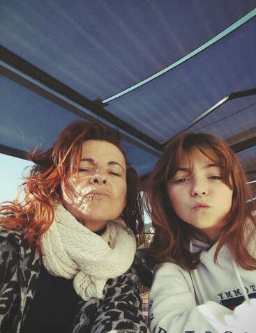 Une femme et une jeune fille aux cheveux roux similaires posent ensemble sous un auvent bleu, faisant des grimaces espiègles à l'appareil photo, bien emmitouflées.