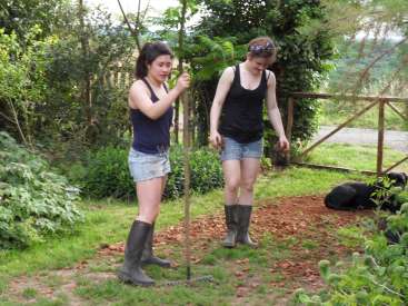 L'image représente deux femmes dans un jardin, vêtues de bottes Wellington et de shorts, l'une tenant un râteau et l'autre se tenant à côté d'elle.