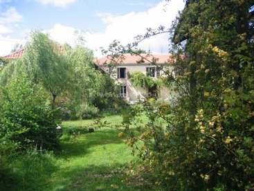 L'image représente une scène sereine d'une maison nichée dans une végétation luxuriante, entourée d'un jardin vibrant et d'arbres, le tout dans un ciel d'un bleu éclatant.