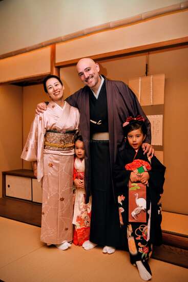 Una sonriente familia de cuatro miembros, vestidos con kimonos tradicionales japoneses, posan juntos en el interior sobre tatamis, creando un momento cultural cálido y alegre.