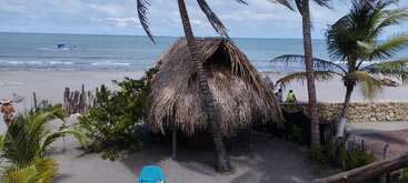 La imagen representa una serena escena playera con una estructura de madera, posiblemente un muelle o embarcadero, rodeada de arena y agua, que evoca una sensación de tranquilidad y relajación.