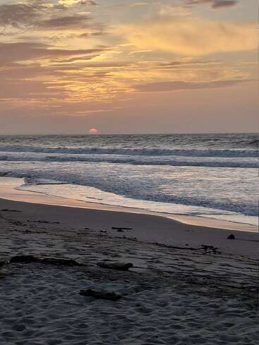 Una serena puesta de sol en la playa, con suaves olas rodando sobre la arena. El cielo brilla suavemente con colores cálidos, creando un ambiente tranquilo y relajante.