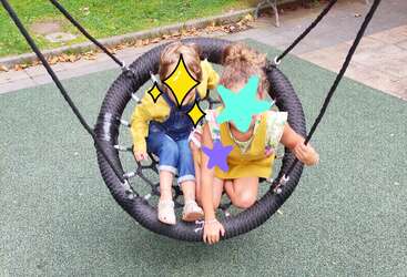 A imagem mostra duas crianças brincando em um playground, com um balanço e um escorregador, cercado por grama verde e árvores, transmitindo uma sensação de diversão e atividade ao ar livre.
