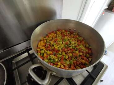 Una gran olla de metal está sobre el fogón llena de coloridos tomates cherry cortados en rojo, amarillo y verde, listos para ser cocinados o preparados más adelante.