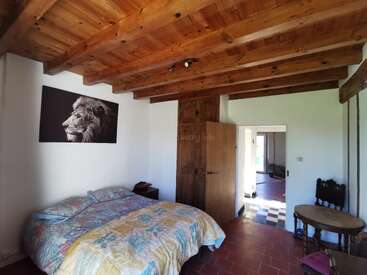 Dieses gemütliche Schlafzimmer verfügt über eine Holzbalkendecke, ein Doppelbett mit bunter Bettwäsche, ein Löwenporträt, Holzmöbel und einen angrenzenden Raum mit kariertem Boden.