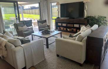 Dieses Wohnzimmer verfügt über zwei Sofas, zwei Sessel, einen Couchtisch, einen großen Fernseher, Lampen, eine Zimmerpflanze, Glasschiebetüren und eine gemütliche, einladende Atmosphäre.