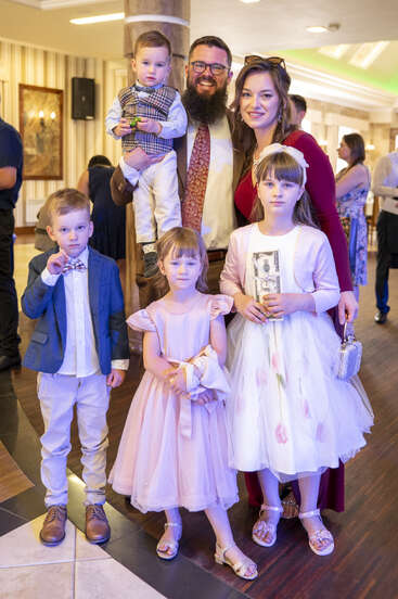 A family of six, including three girls and two boys, pose together indoors. Everyone is dressed formally, smiling, and ready for a festive celebration.