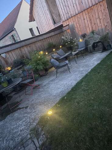 L'image représente un patio serein, avec une table et des chaises, une pelouse verdoyante et une clôture en bois, dégageant une atmosphère chaleureuse et accueillante.