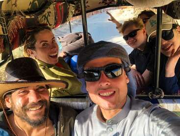 Eine Gruppe lachender Freunde mit Sonnenbrillen und Hüten macht fröhlich ein Selfie in einem Auto, vielleicht auf einem lustigen Outdoor-Abenteuer oder Roadtrip.