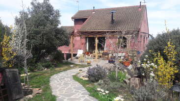 The image depicts a charming red house with a brown tiled roof, surrounded by a stone pathway and lush greenery, exuding a sense of serenity and tranquility.