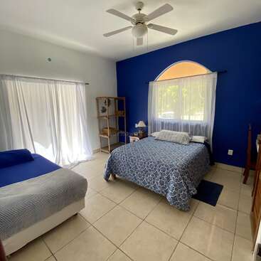 The image depicts a serene bedroom with two beds, a blue accent wall, and a large window, exuding a sense of calmness and tranquility.