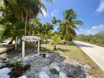 The image depicts a tropical scene with palm trees, a road, and a sign reading \"Casa Jamila\" in a serene and natural setting.