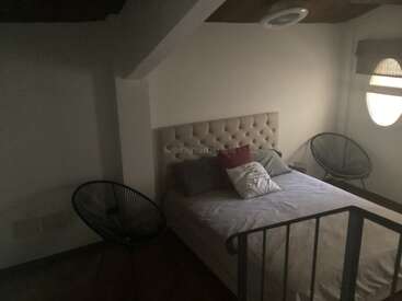 Cette chambre à coucher confortable est dotée d'une tête de lit touffetée, d'un lit soigneusement fait avec des oreillers, de deux chaises rondes modernes, d'un éclairage doux et d'une fenêtre circulaire qui apporte de la lumière naturelle.