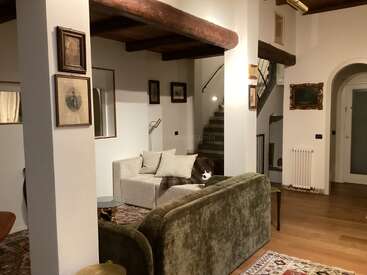 Ce salon confortable présente des poutres en bois apparentes, des œuvres d'art vintage encadrées, un canapé en velours vert, un canapé crème, des planchers en bois et un escalier avec une rampe en métal.