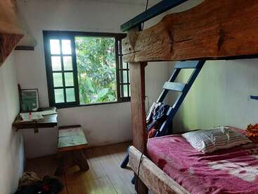 La imagen muestra una acogedora habitación con una litera, con una escalera y un marco de madera, acompañada de una ventana, un banco y un escritorio, que desprenden un ambiente rústico y natural.
