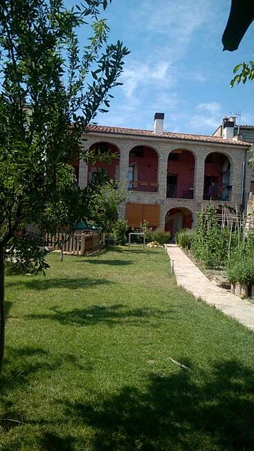 The image depicts a two-story house with arched windows and doors, a chimney, and a balcony, surrounded by lush greenery and a serene blue sky.