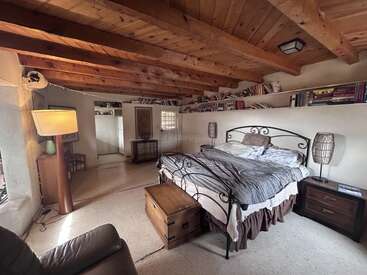 Dieses gemütliche Schlafzimmer hat ein schmiedeeisernes Bett, Holzbalken an der Decke, Nachttische, Bücherregale, sanfte Beleuchtung, einen Vintage-Koffer und eine natürliche, rustikale Einrichtung.