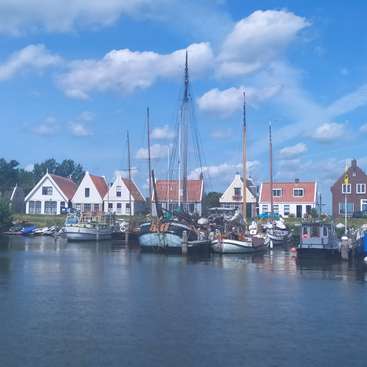 The image depicts a serene scene of a small harbor with boats docked, surrounded by houses and a blue sky with clouds, evoking a sense of tranquility.