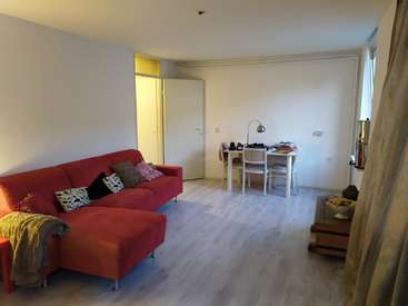 The image depicts a living room with a red couch, white desk, and wooden floor, featuring a doorway, window, and lamp, with a subtle watermark in the center.