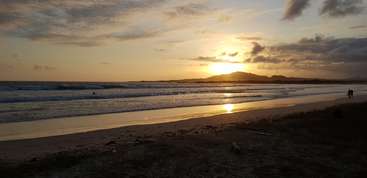 La imagen representa una serena escena playera con un mar en calma, una orilla arenosa y un cielo despejado, que evoca una sensación de tranquilidad y relajación. El ambiente es apacible e idílico.