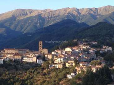L'image représente une petite ville nichée dans les montagnes, avec un clocher d'église proéminent et une chaîne de montagnes en arrière-plan.