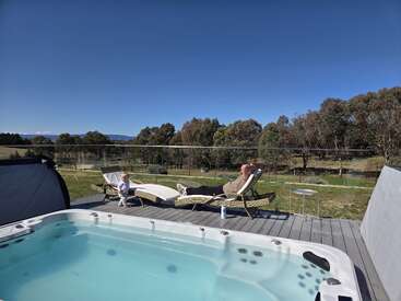 Ein Mann und ein Kind entspannen sich auf Liegestühlen an einem Whirlpool und genießen einen sonnigen Tag mit einer malerischen Landschaft und einem bewaldeten Hintergrund. Friedliche, heitere Atmosphäre.