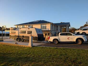 Ein modernes zweistöckiges Haus ist bei Sonnenuntergang abgebildet, mit einem großen Wohnwagen und einem weißen Pickup, der in der Einfahrt neben einem Basketballkorb steht.