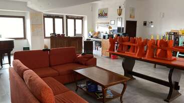 This image shows a spacious, well-lit living room with red sofas, a wooden coffee table, a grand piano, a dining table with chairs stacked atop it.