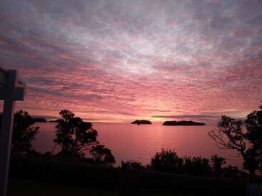 Una impresionante puesta de sol llena el cielo de vibrantes tonos rosas y morados, enmarcando las tranquilas aguas, las siluetas de los árboles y las pequeñas islas en el sereno horizonte.
